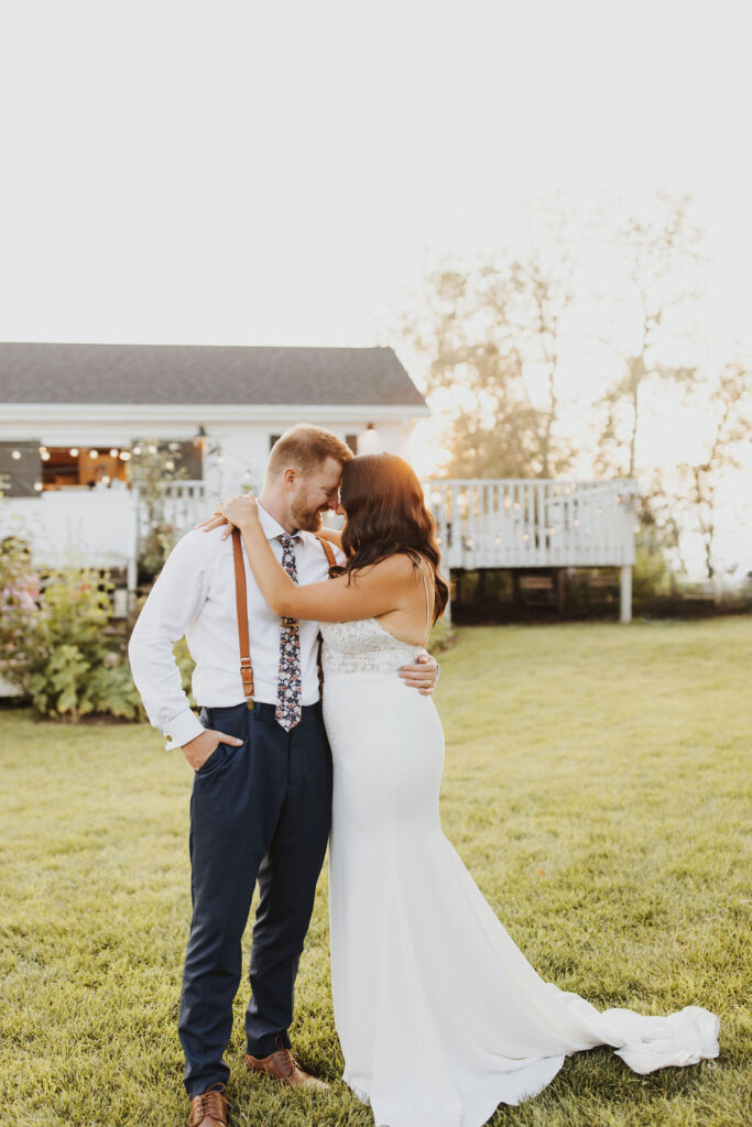 A bride and groom embracing in front of venue house at sunset.