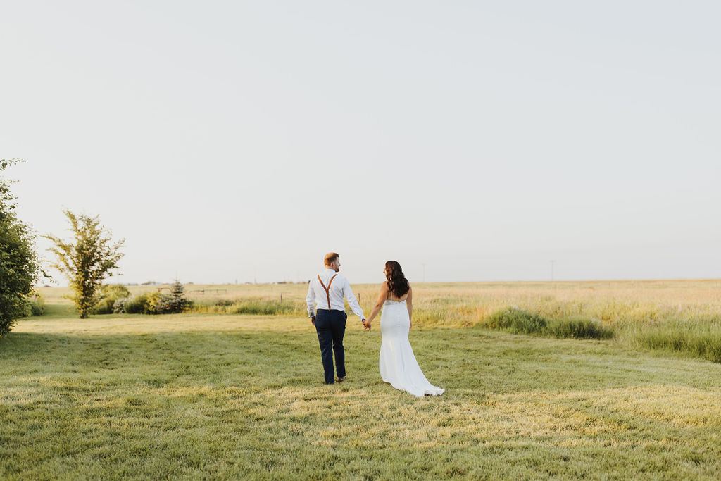 A bride and groom walking through a grassy field. The Gathered outdoor wedding and events venue.