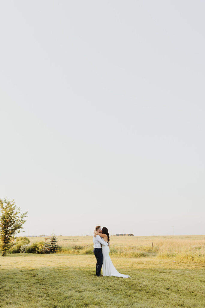 A bride and groom embrace in a field at sunset. The Gathered outdoor wedding and events venue.