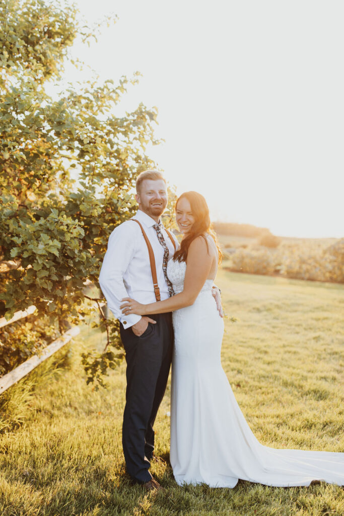A bride and groom standing in an orchard at sunset. The Gathered outdoor wedding and events venue.