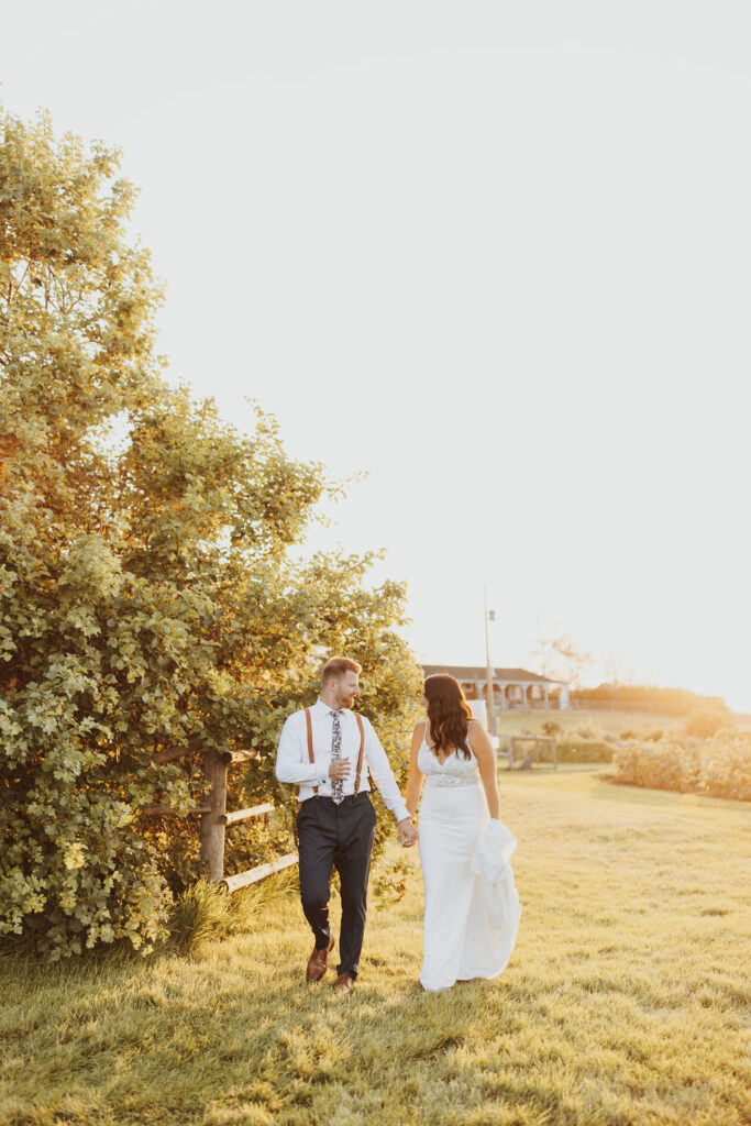 A bride and groom walking through a field at sunset. The Gathered outdoor wedding and events venue.