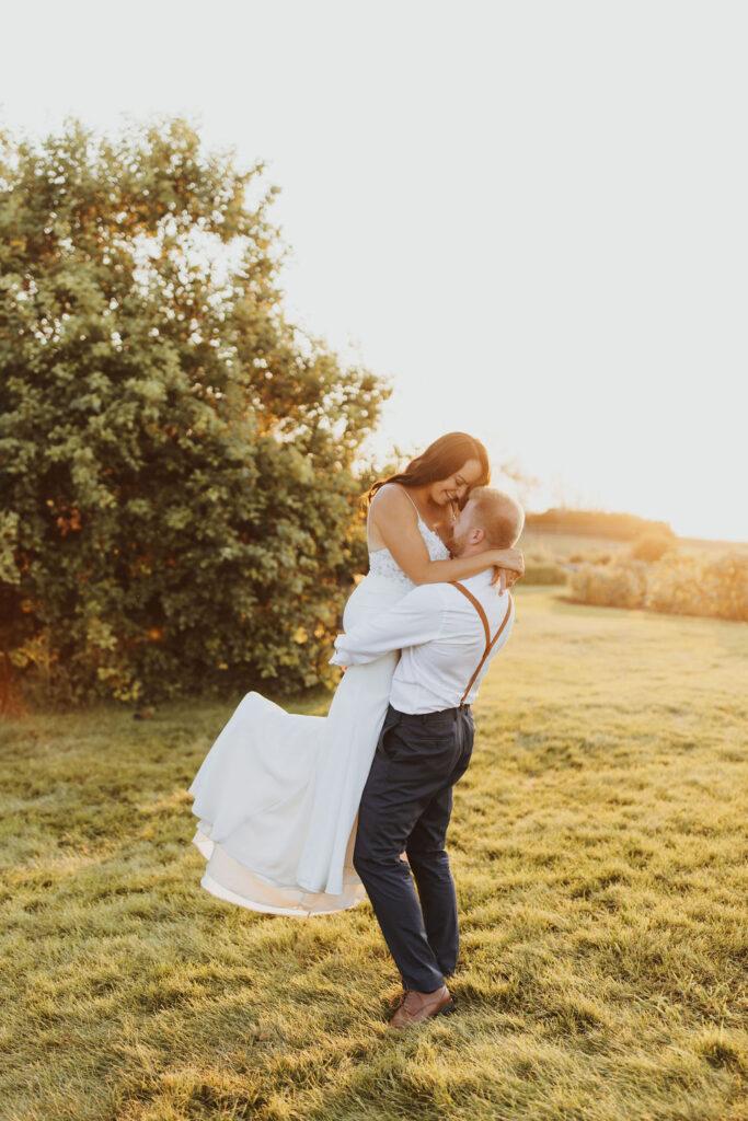 A bride and groom hugging in a field at sunset. The Gathered outdoor wedding and events venue.