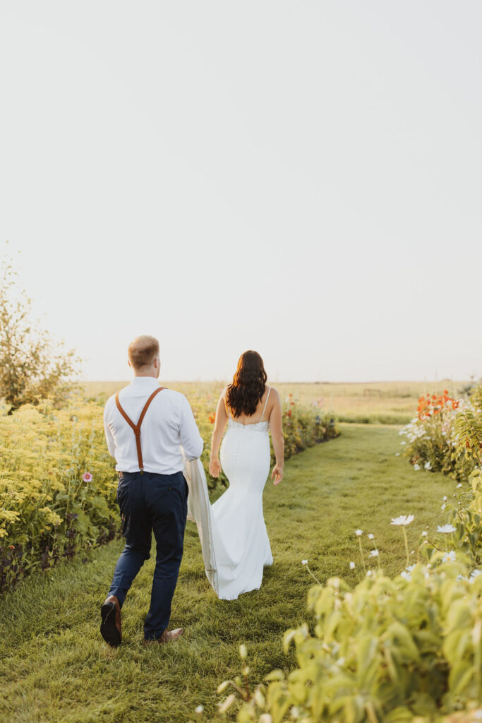 A bride and groom walking through a field of flowers at The Gathered outdoor wedding and events venue.