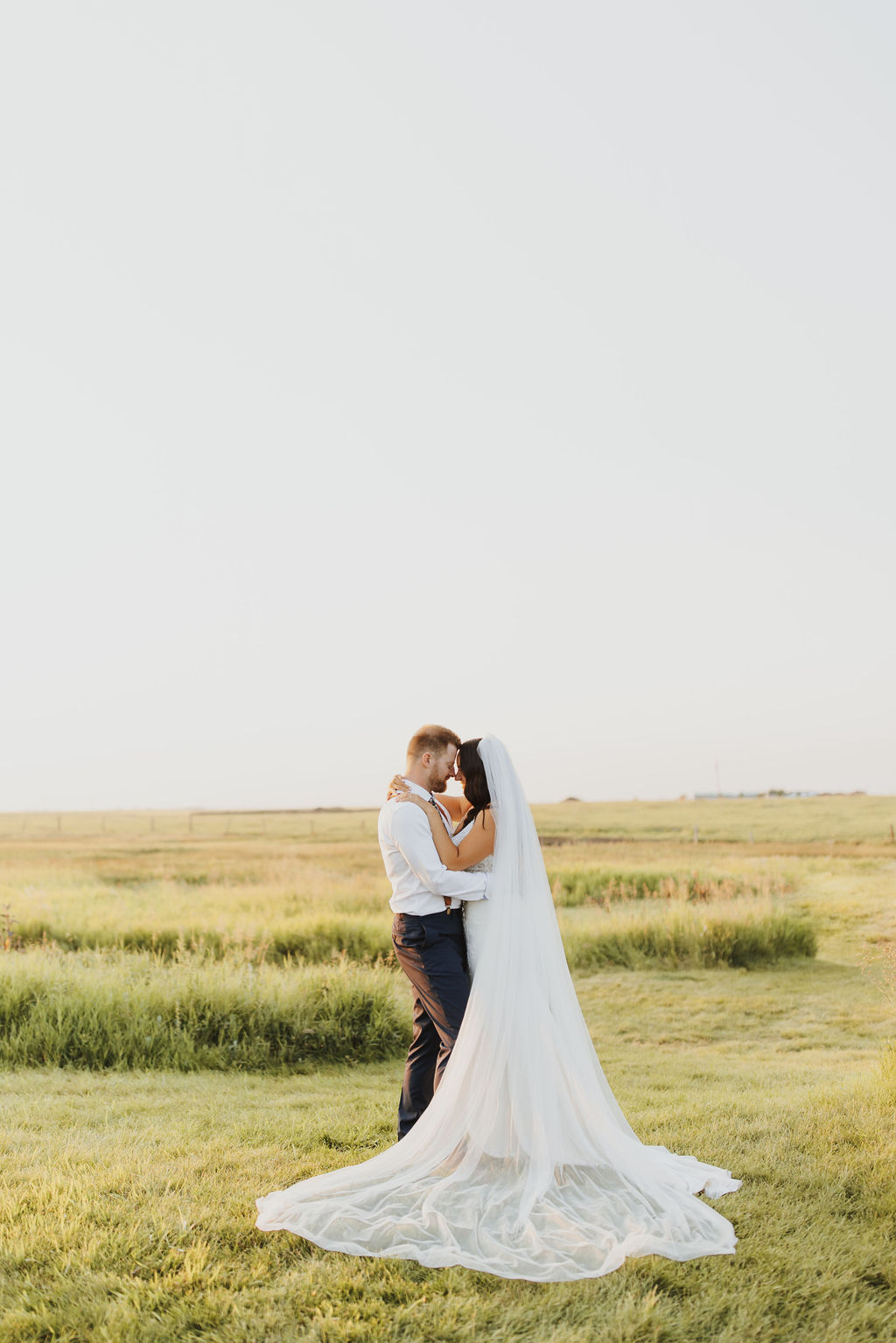 A bride and groom embrace in a grassy field.