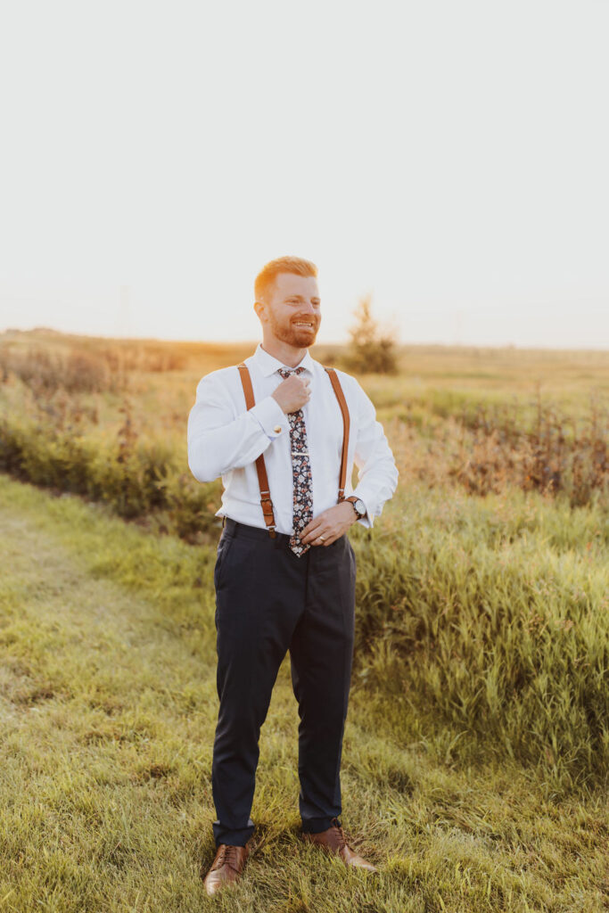A man in suspenders standing in a field at sunset.