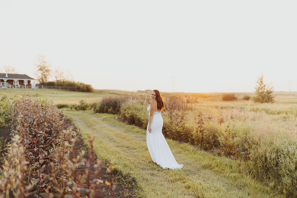 A bride in a white dress walks through a field at sunset.