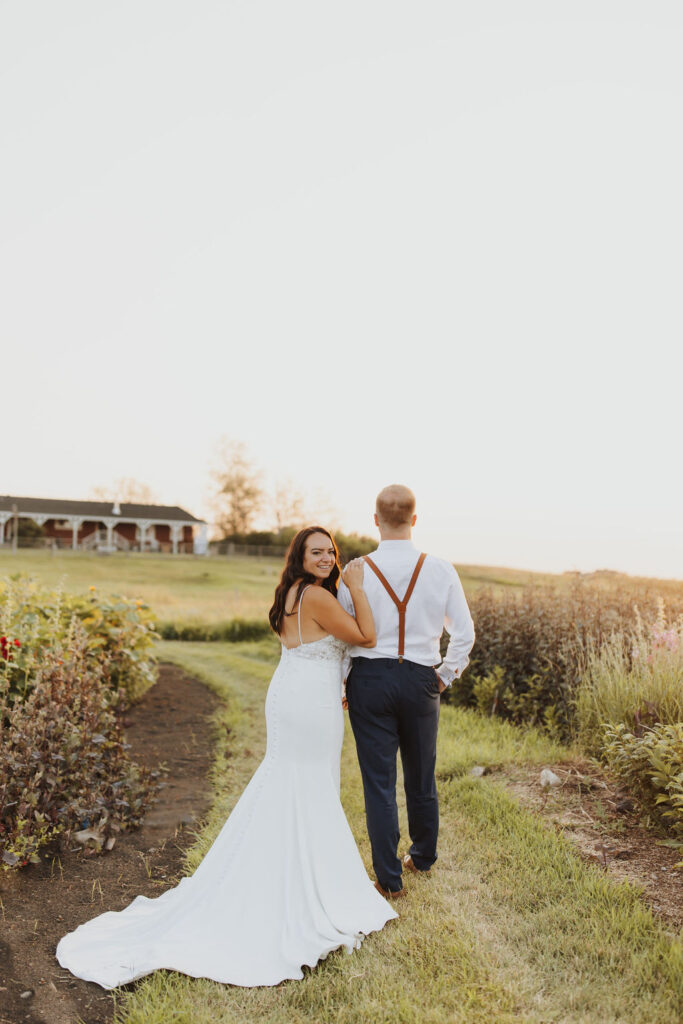 A bride and groom walk through a field at sunset.
