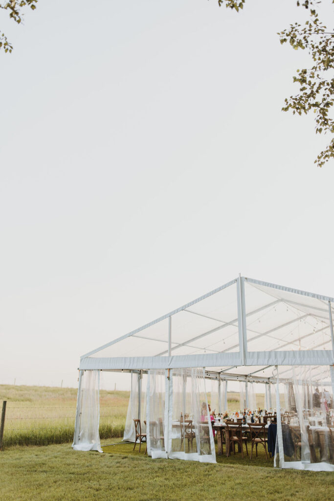 A clear tent with tables and chairs in a field. Enchanting Outdoor Dinner Party with long wedding tables.