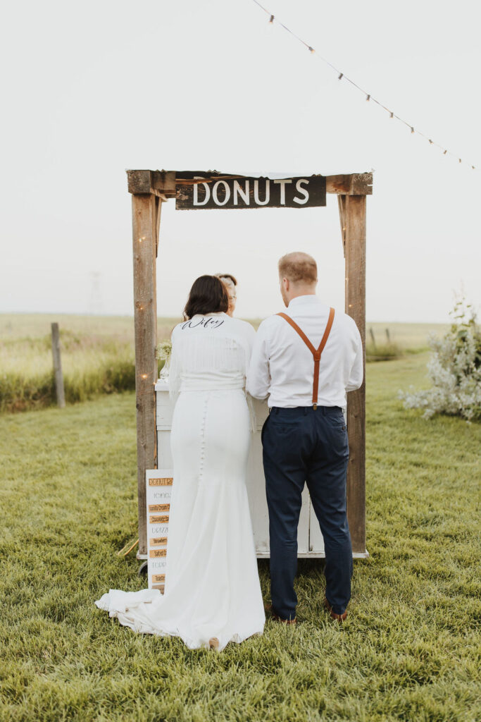 A bride and groom standing in front of a donut cart. Enchanting Outdoor Dinner Party.