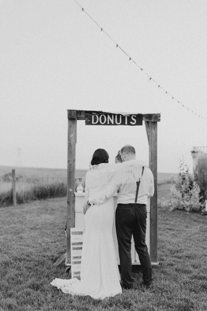 A bride and groom standing in front of a donut sign.
