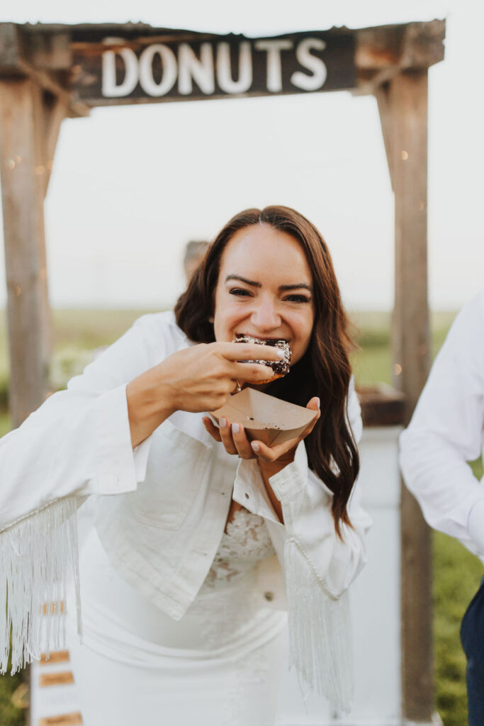 A bride and groom eating donuts in front of a sign.