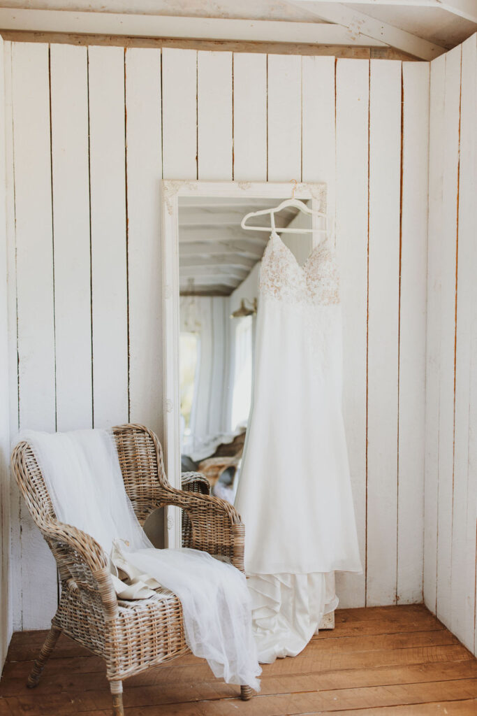 A wedding dress hangs on a chair in a room with white walls.