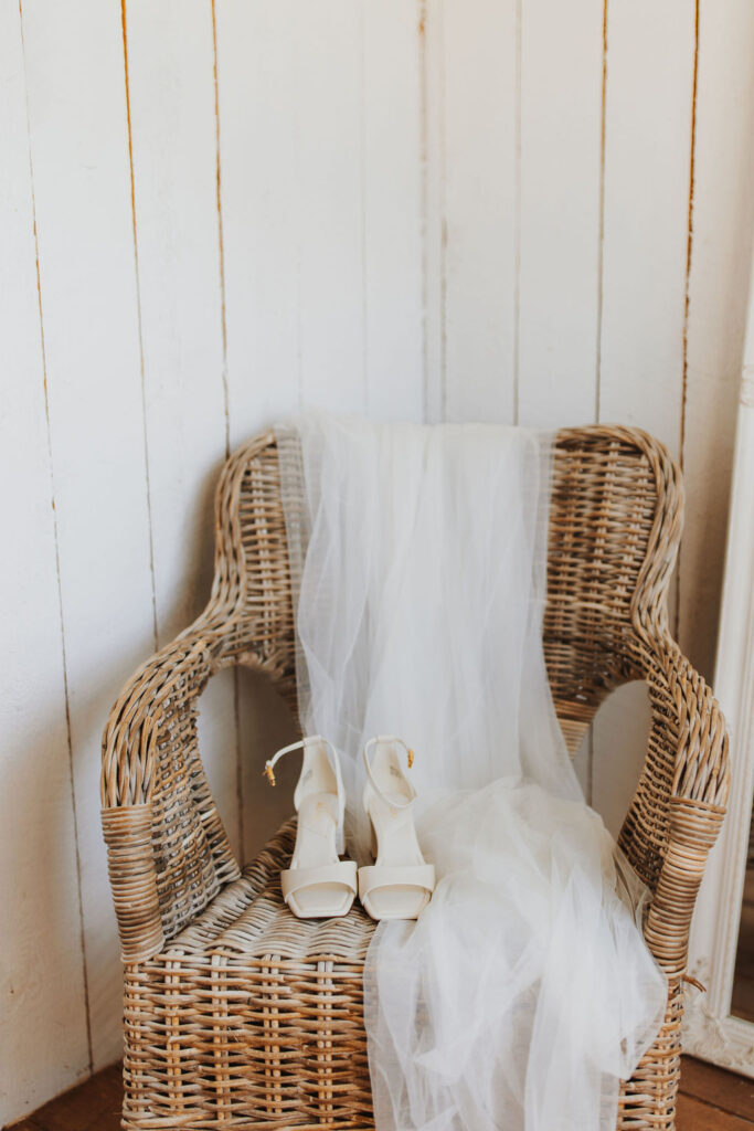 A wicker chair with wedding shoes on it.