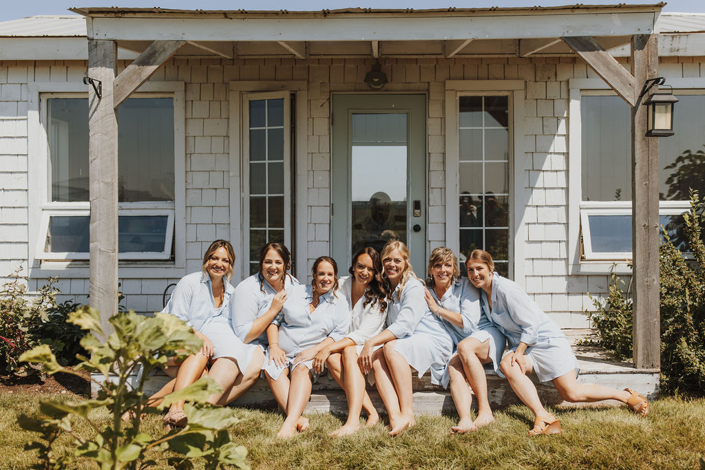 A group of bridesmaids in blue robes posing in front of a house.
