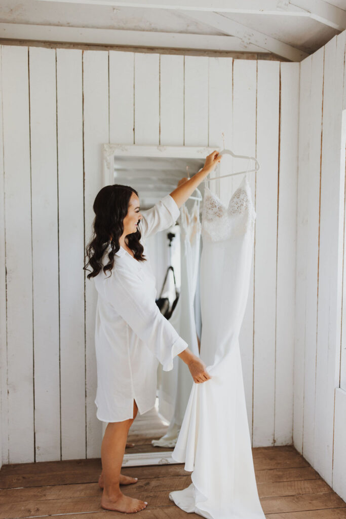 A bride putting her wedding dress on a hanger in a white room.