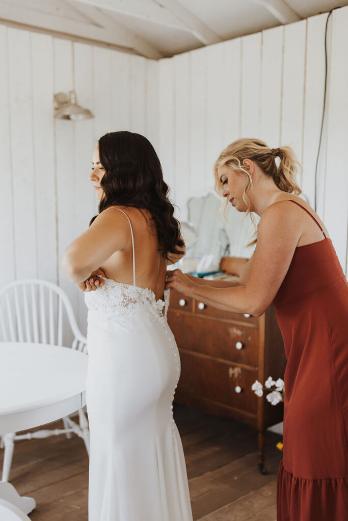 A bride is getting ready in a room with a bridesmaid.