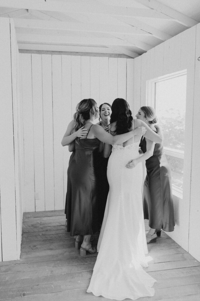 A bride and her bridesmaids hugging in a room.