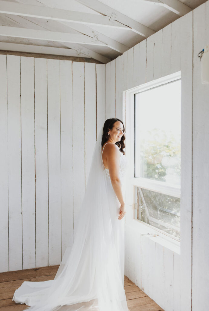 A bride in a white wedding dress standing in front of a window.