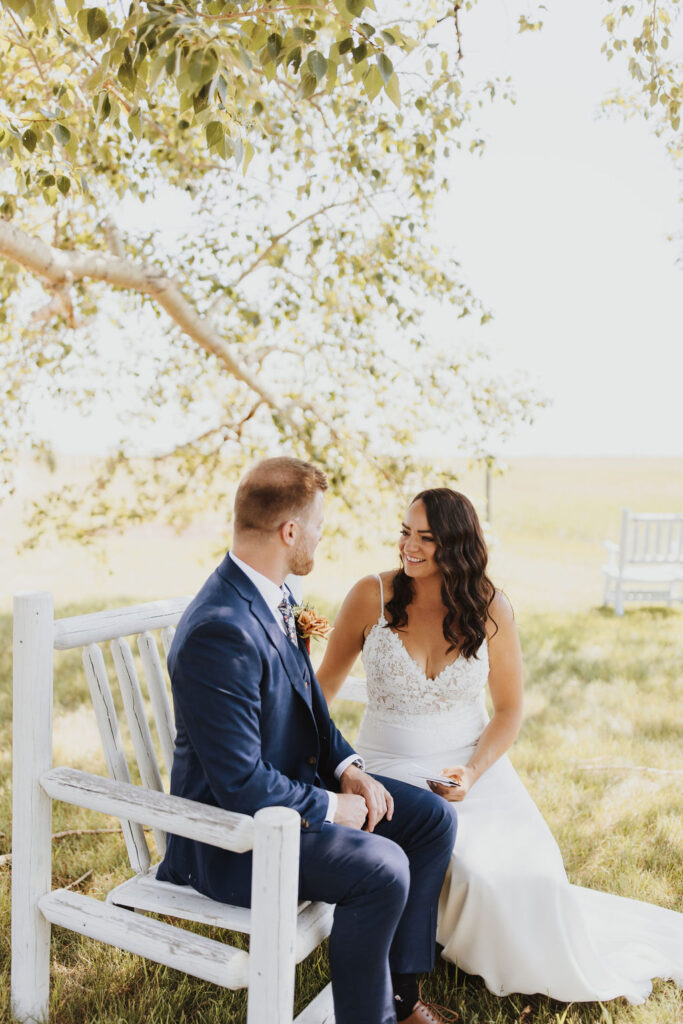 A bride and groom sitting on a bench in a field. Outdoor Dinner Party
