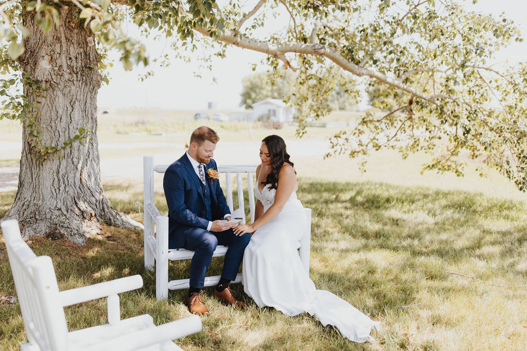 A bride and groom sitting on a bench under a tree.