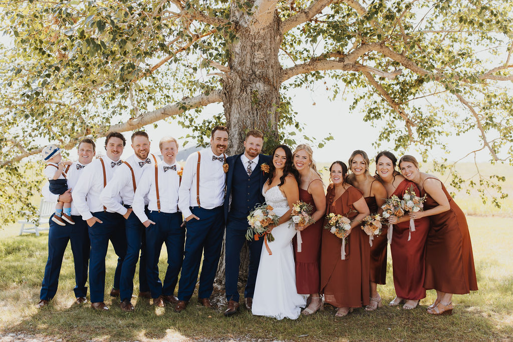A group of bridesmaids and groomsmen posing in front of a tree. Outdoor Dinner Party