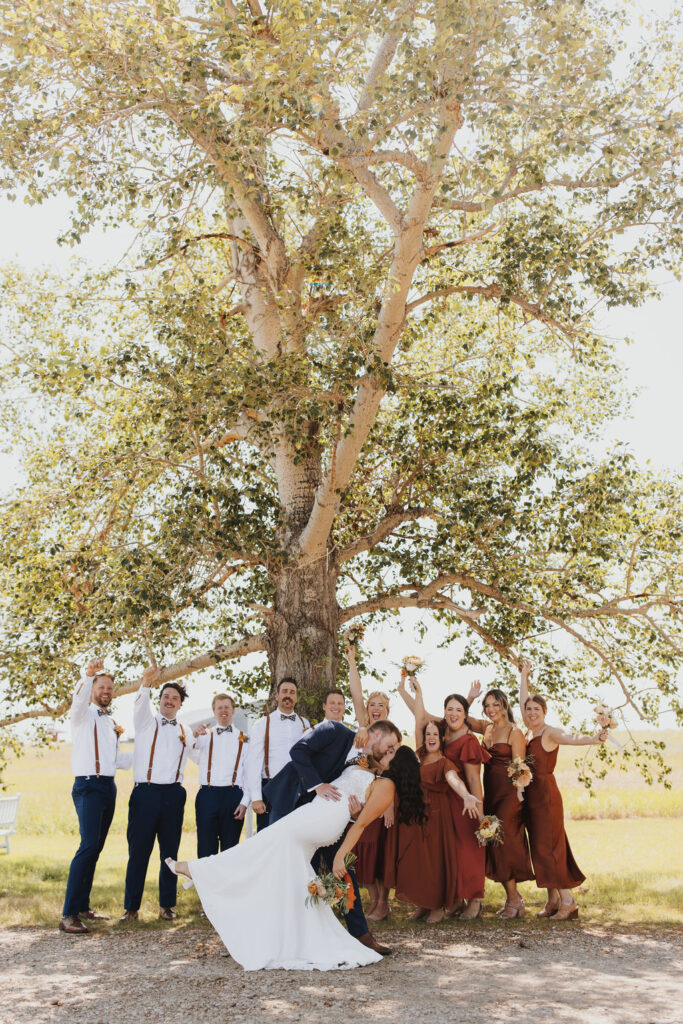 A group of bridesmaids and groomsmen kissing in front of a tree.