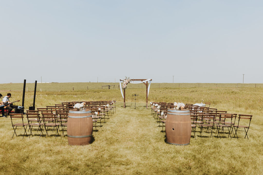 A wedding ceremony set up in a field with chairs and barrels.