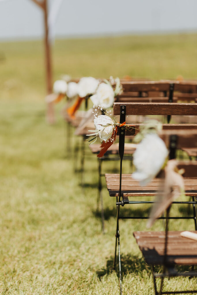 A row of wooden chairs in a field with flowers on them.