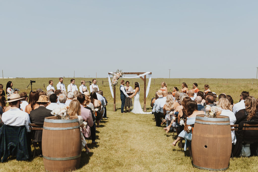A wedding ceremony in a field with barrels in the background.