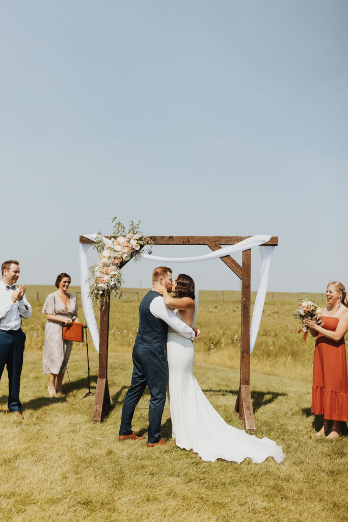 A bride and groom kiss in the middle of a field.