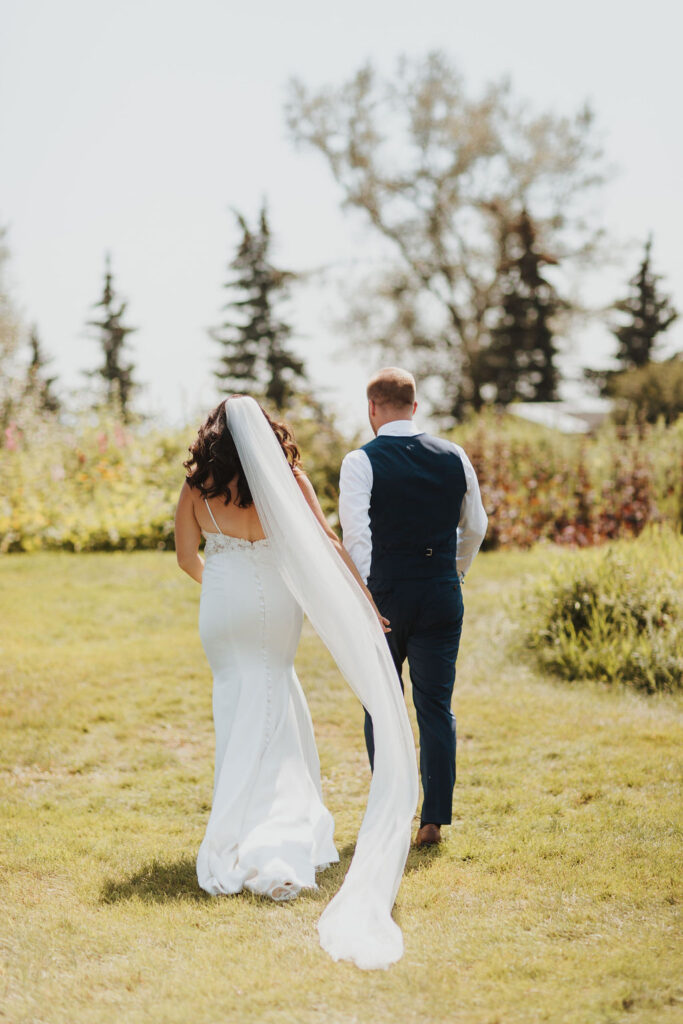 A bride and groom walking through a grassy field.