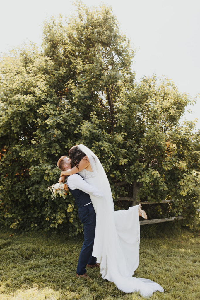 A bride and groom hugging in front of a tree.