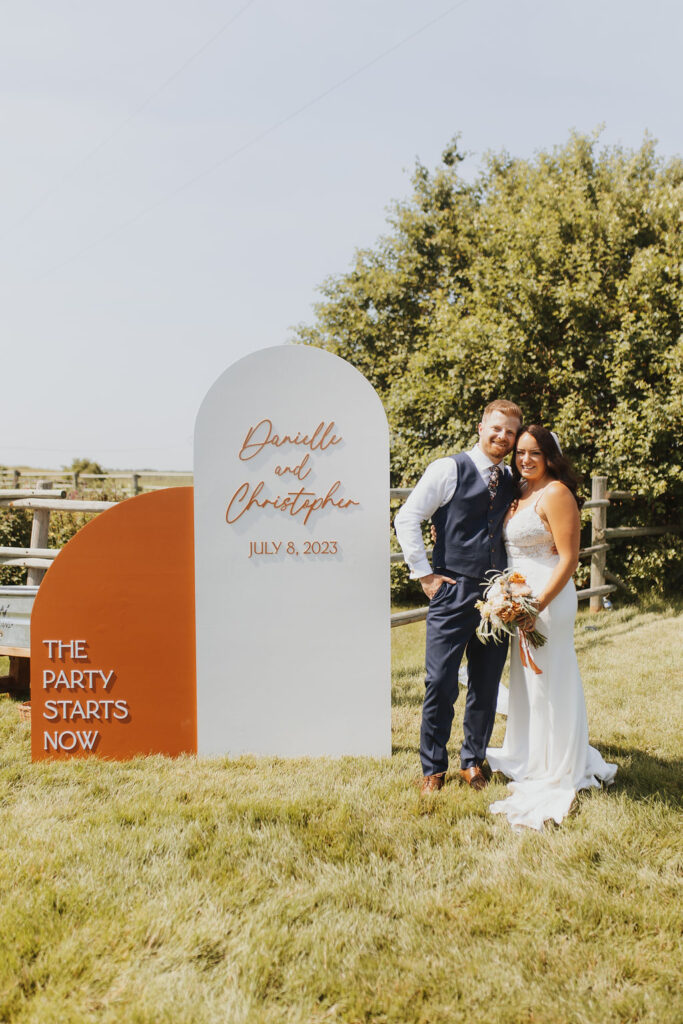 A bride and groom standing in front of an orange sign.