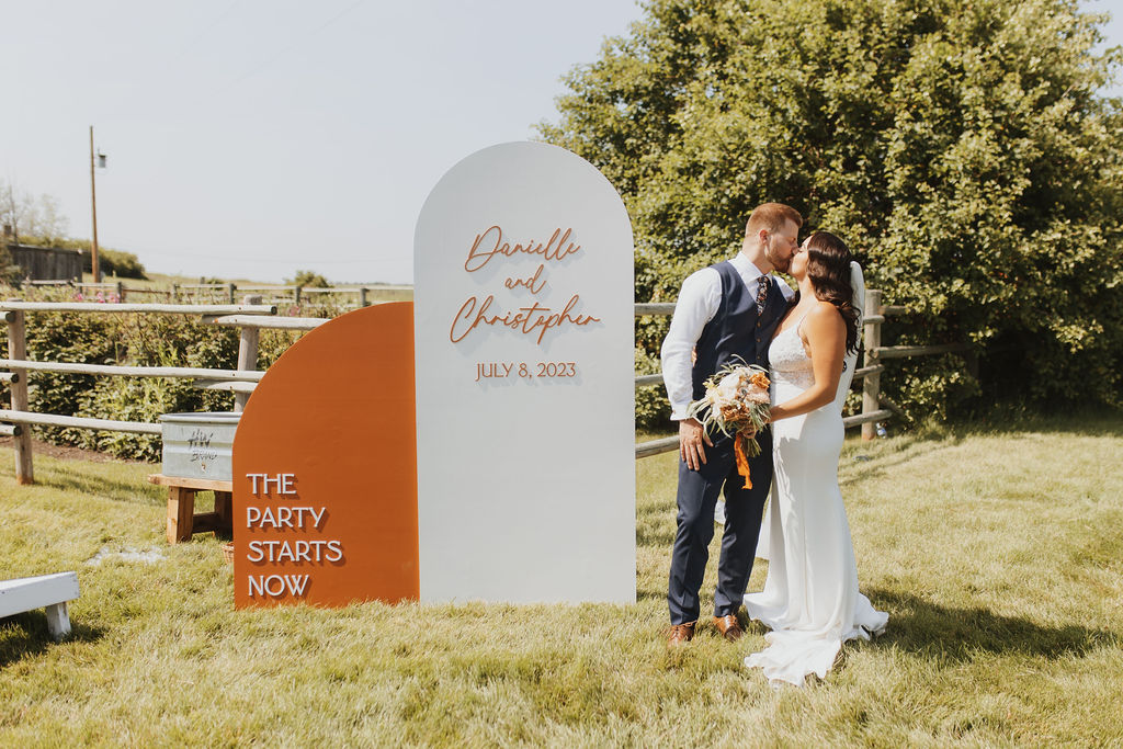A bride and groom kissing in front of an orange and white sign.