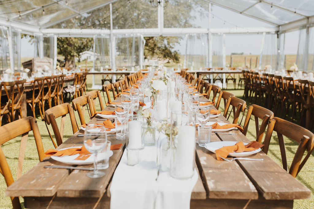 A long table set for a wedding party with hurricane candles, and rust napkins. Outdoor Dinner Party