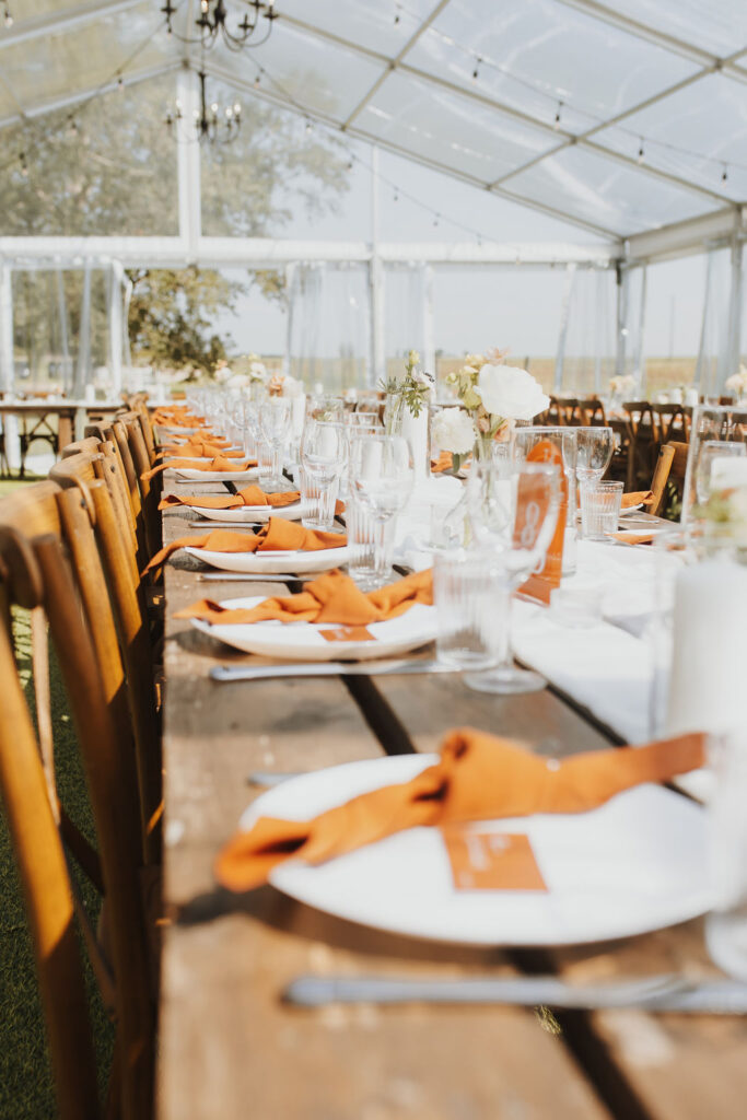 A table set up in a tent with orange napkins. Outdoor Dinner Party