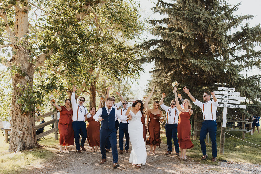 A group of bridesmaids and groomsmen standing on a dirt road.