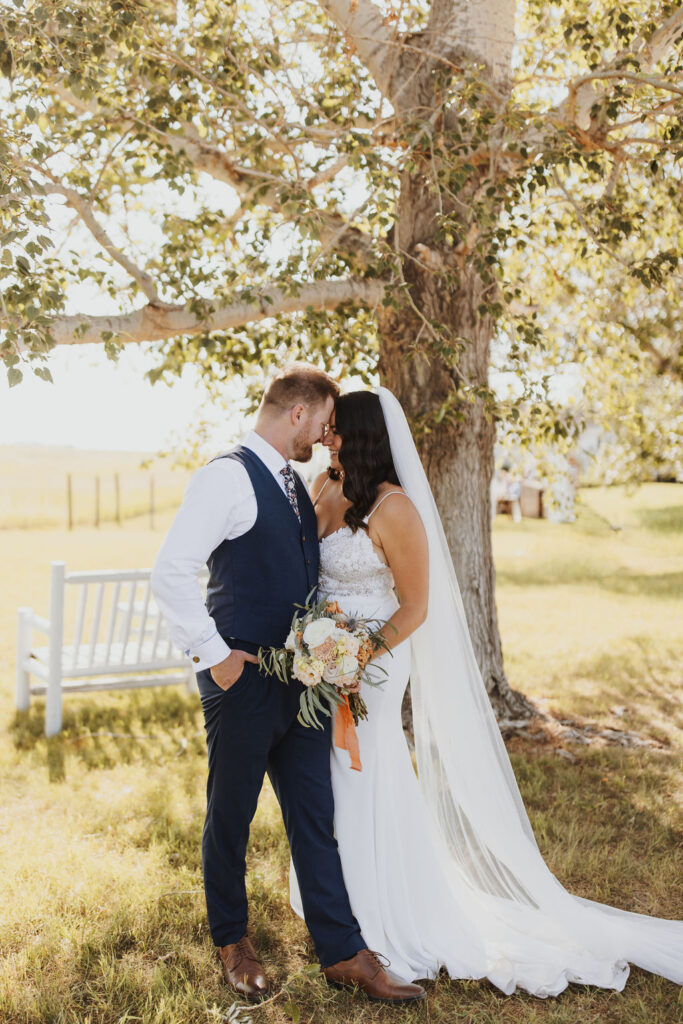 A bride and groom kissing under a tree in a field.