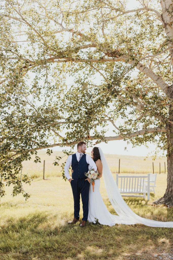 A bride and groom standing under a large tree.