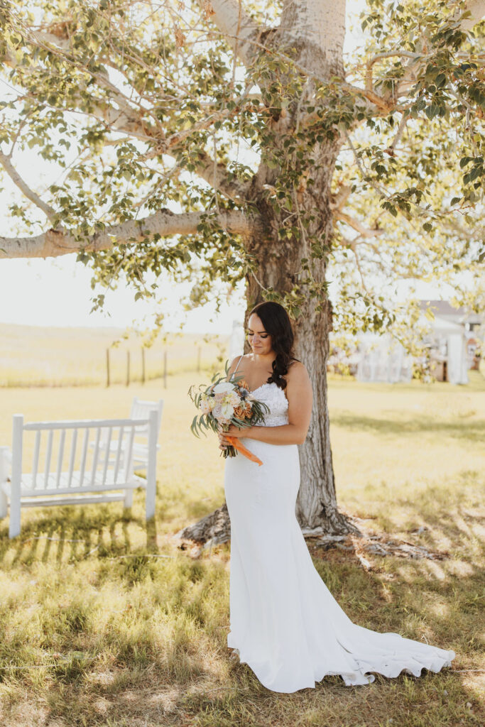 A bride in a white dress standing under a tree.