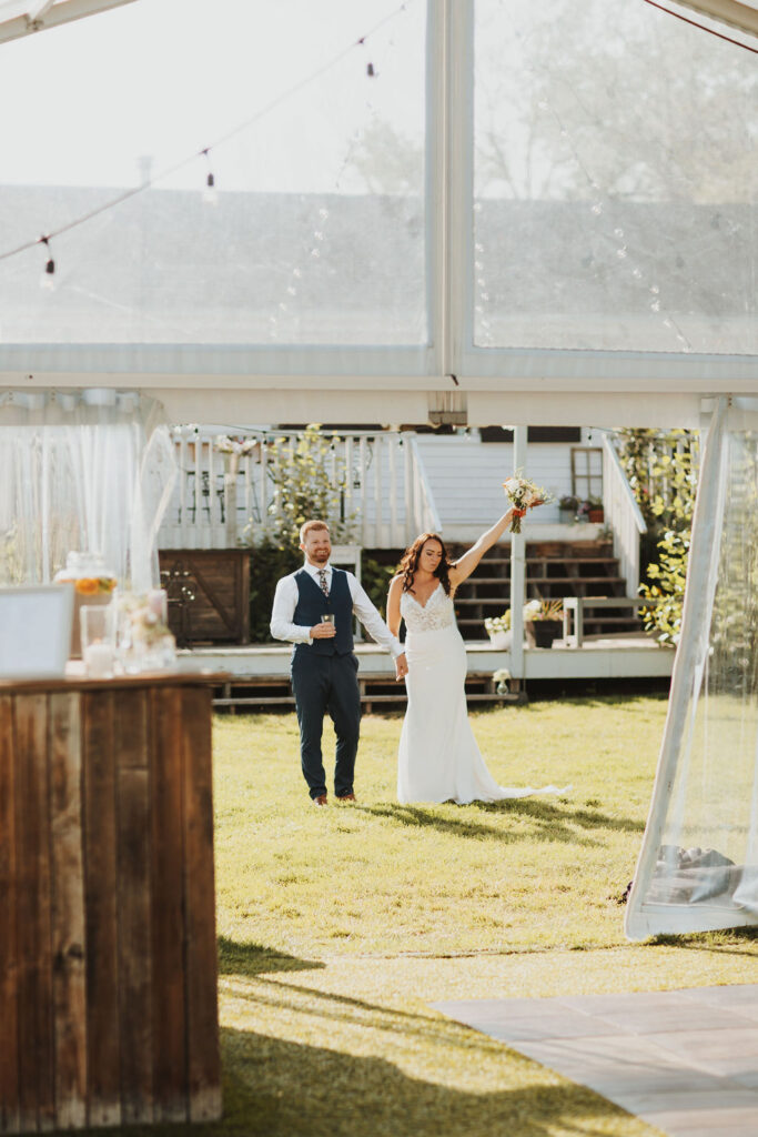 A bride and groom walk through a tent at their wedding reception.