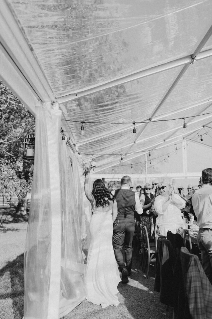 A bride and groom walking down the aisle in a tent.