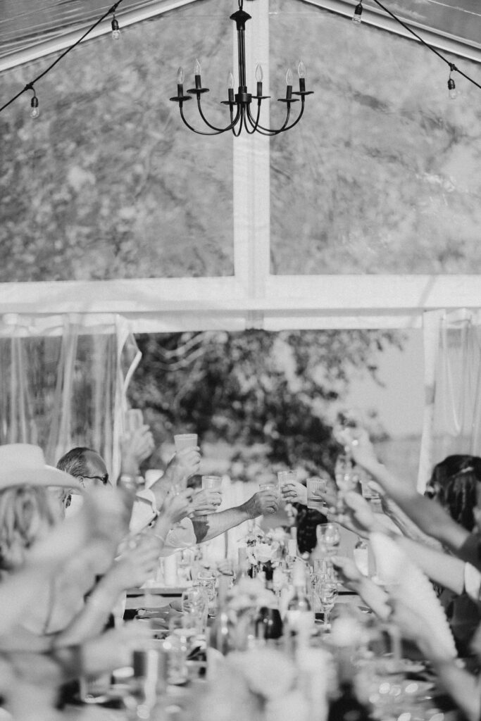 A black and white photo of people toasting in a tent.