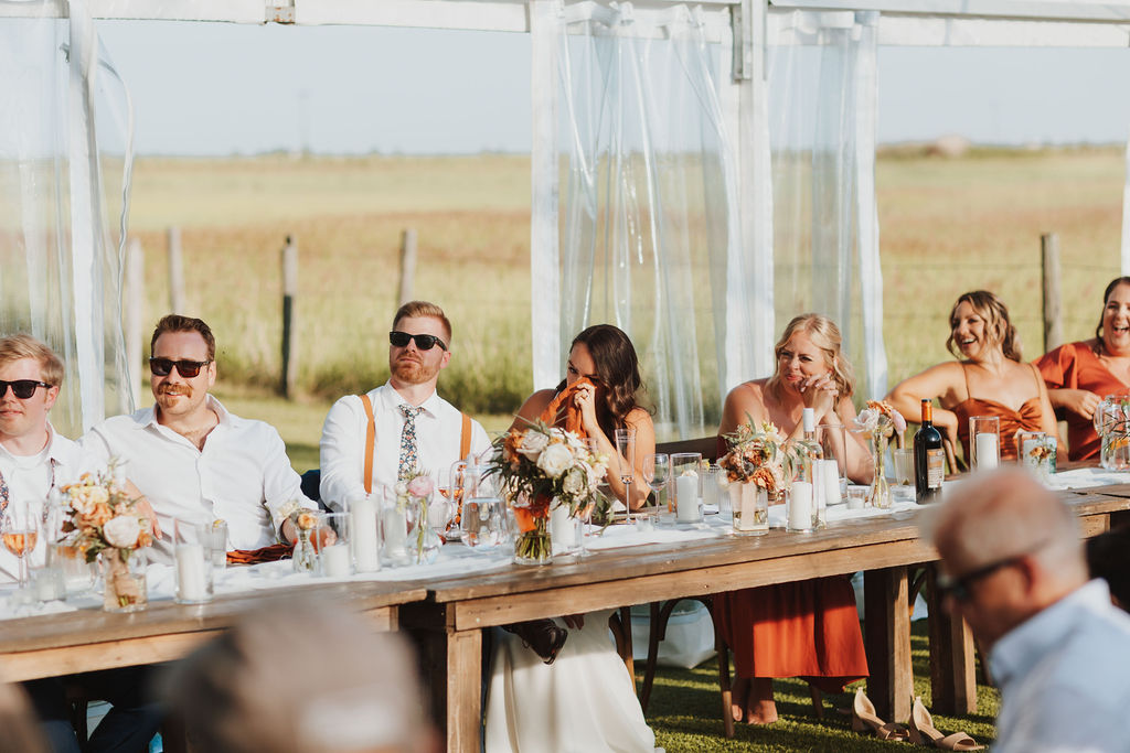 A group of people sitting at a long table at an outdoor wedding.