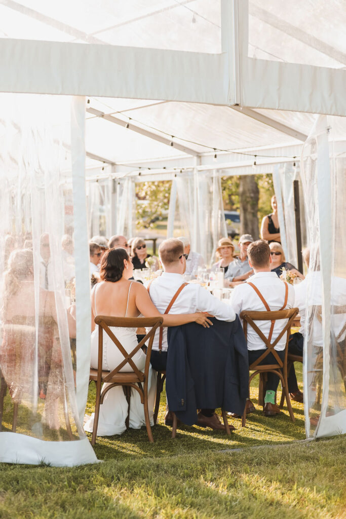 A group of people sitting in a tent at a wedding reception.