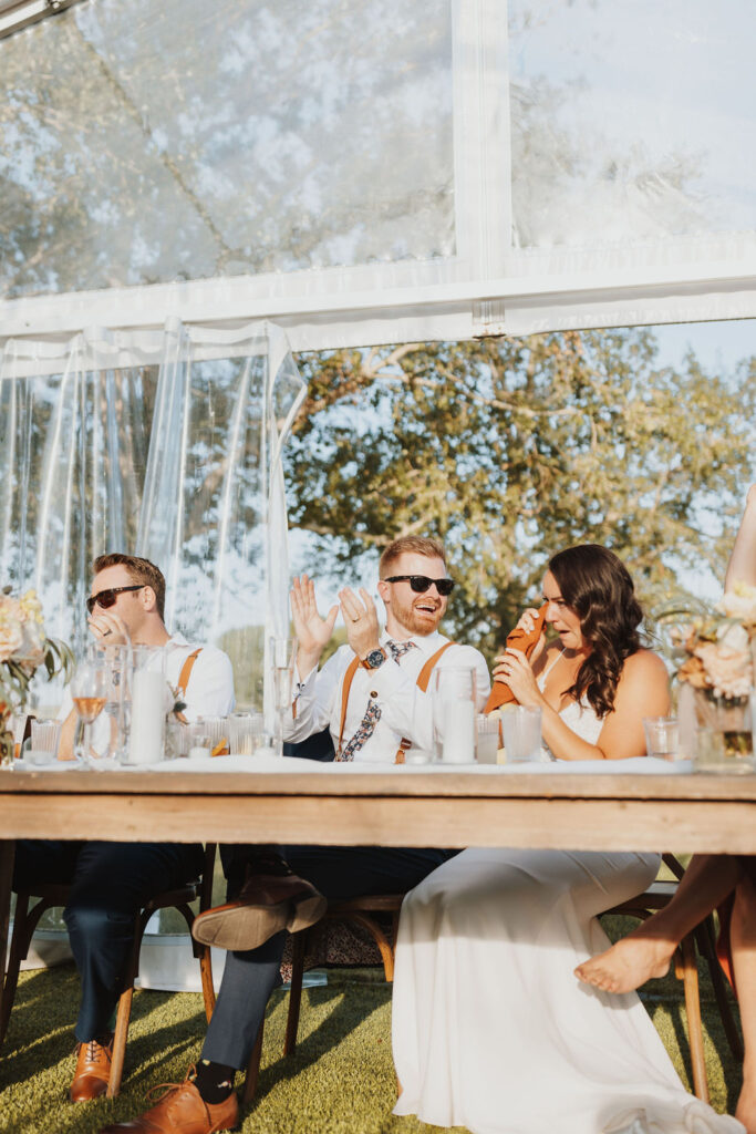 A group of bridesmaids and groomsmen sitting at a table in a tent.