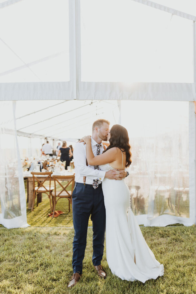A bride and groom kiss in front of a tent.