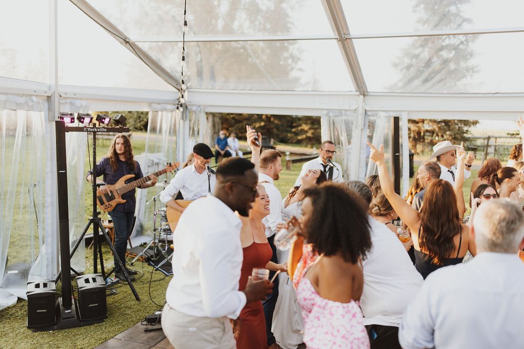 A group of people dancing at a wedding reception in a tent.