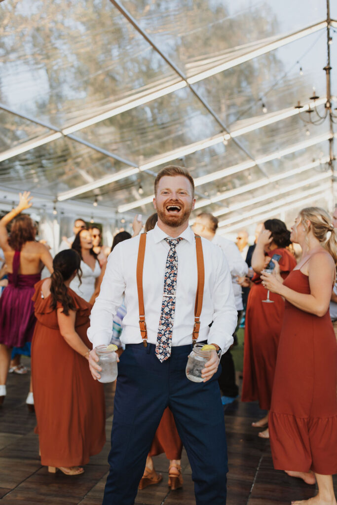 A man in suspenders dancing with a group of people in a tent.