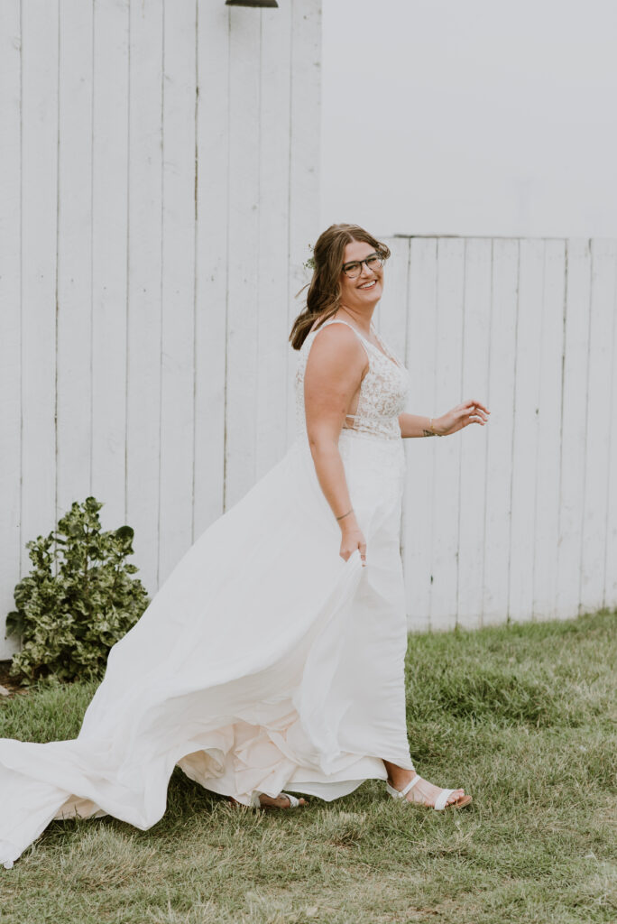 A bride in a white wedding dress walking in front of a white barn.